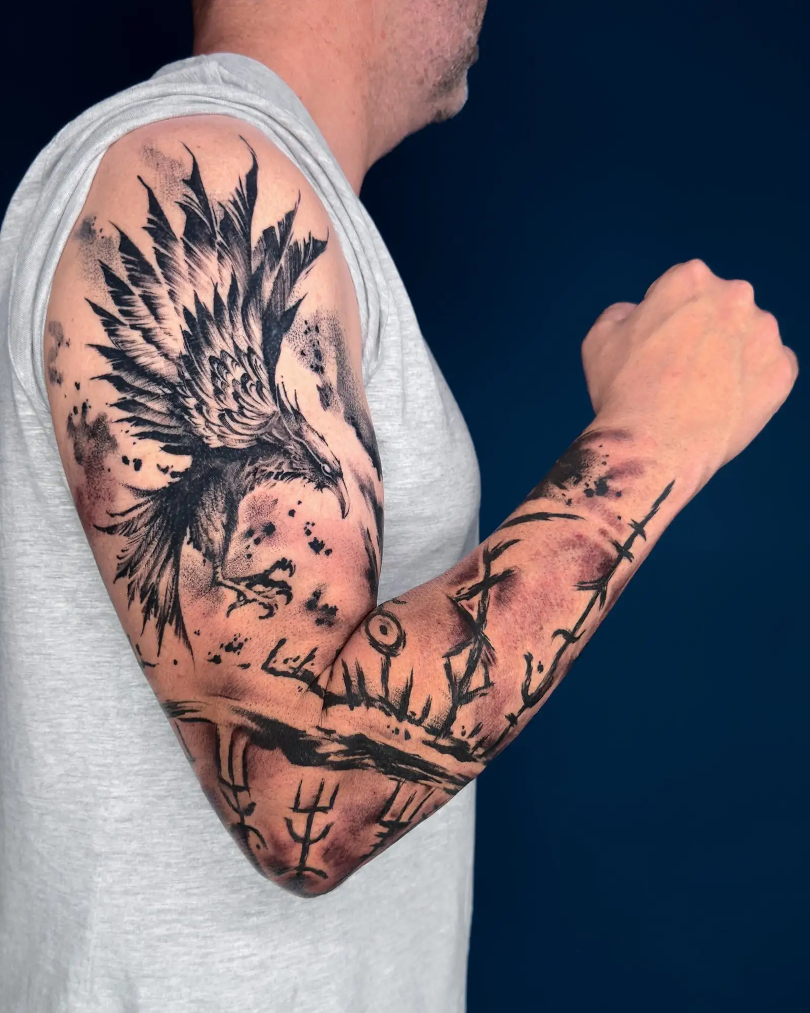 Ein Mann mit einem schwarzen Adler-Tattoo und Runen auf dem Arm.