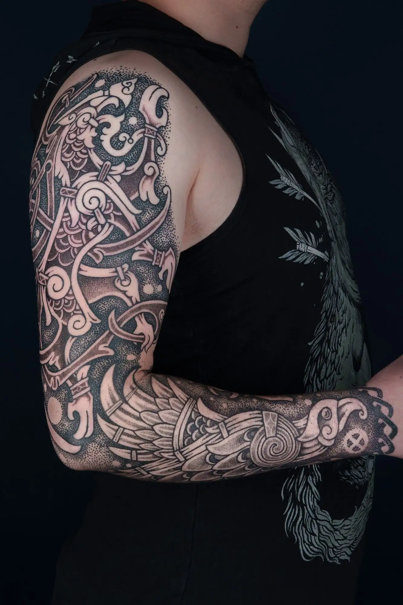 Ein Arm eines Mannes mit einem detaillierten, schwarz-grauen nordischen Tattoo, das den ganzen Arm bedeckt.