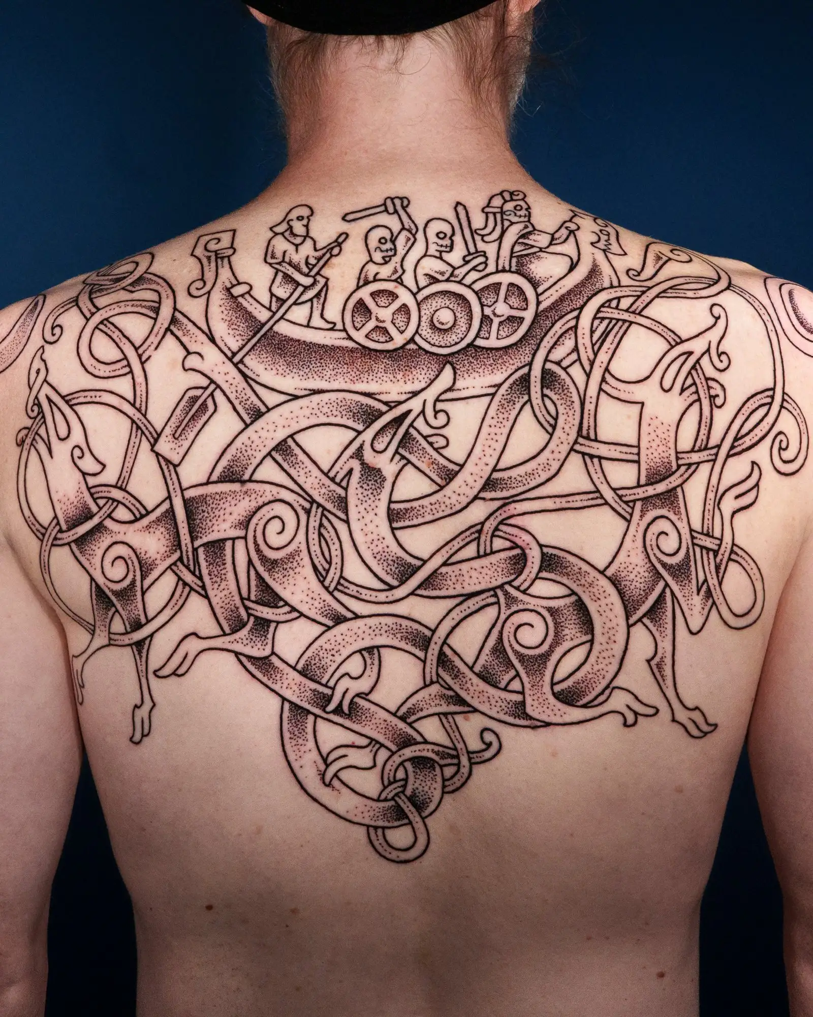 Rücken-Tattoo im nordischen Stil mit einem Drachenboot voller Krieger, umgeben von verschlungenen Mustern und Tieren.