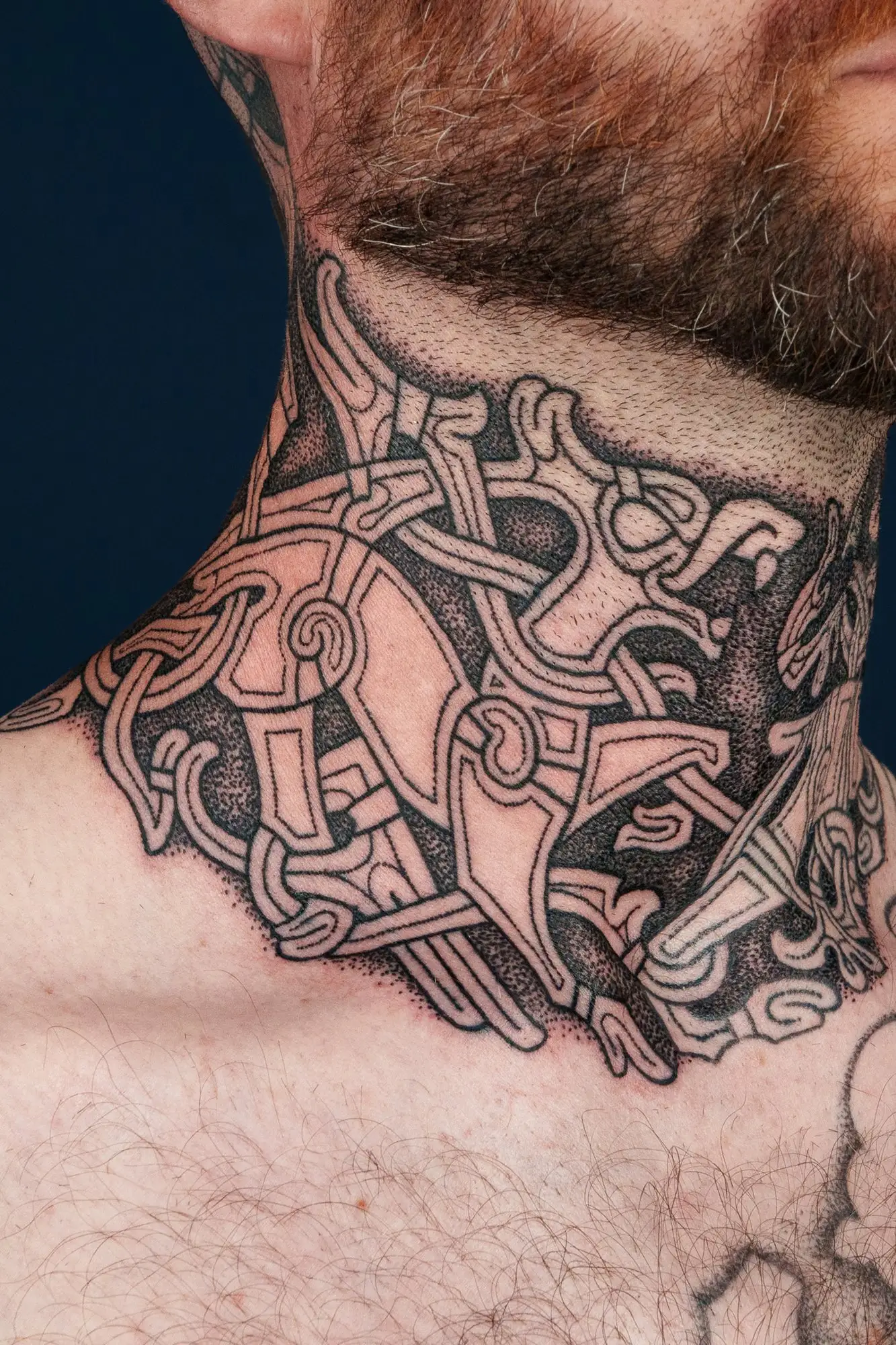Detailansicht eines Mannes mit Bart und einem wikingerzeitlichen Knoten-Tattoo am Hals.