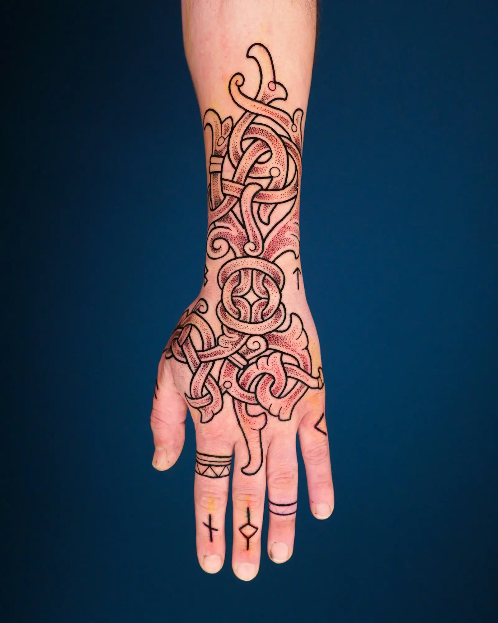 Eine Hand mit einem komplexen, ineinander verschlungenen Tattoo im keltischen Stil, das sich vom Handgelenk bis zu den Fingern erstreckt.