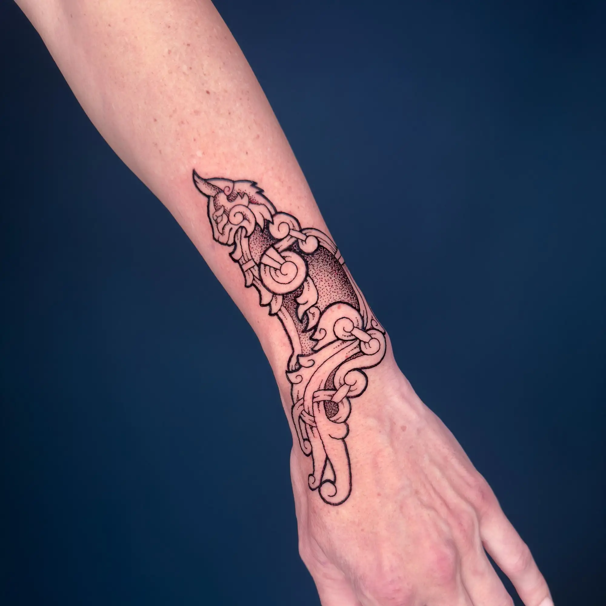 Ein detailliertes schwarzes Wikinger-Tattoo, das eine Katze mit verschlungenen Mustern auf dem Unterarm darstellt.
