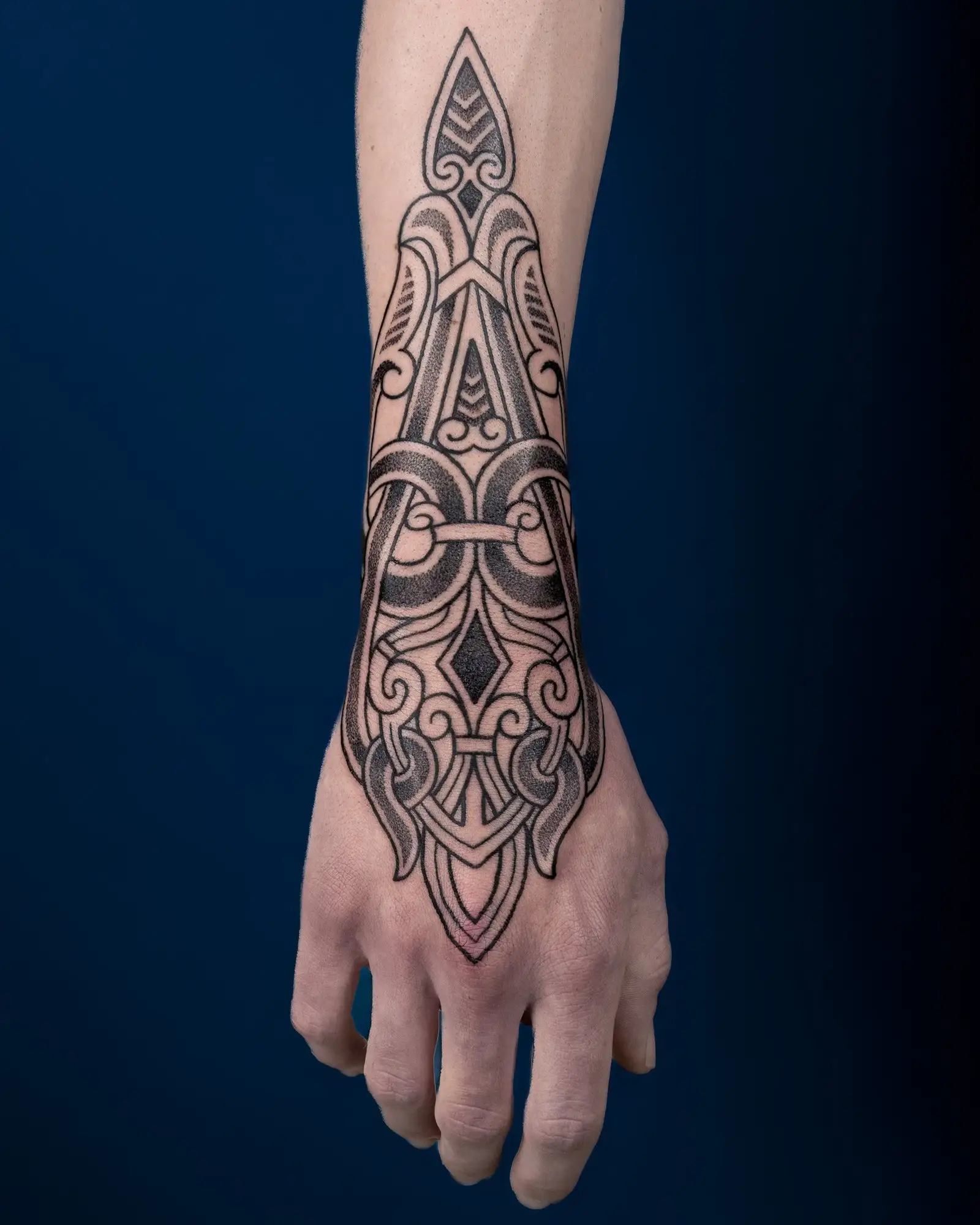 Detailansicht eines Unterarms und Handrückens mit einem großen, komplexen, schwarzen, geometrischen Tattoo.