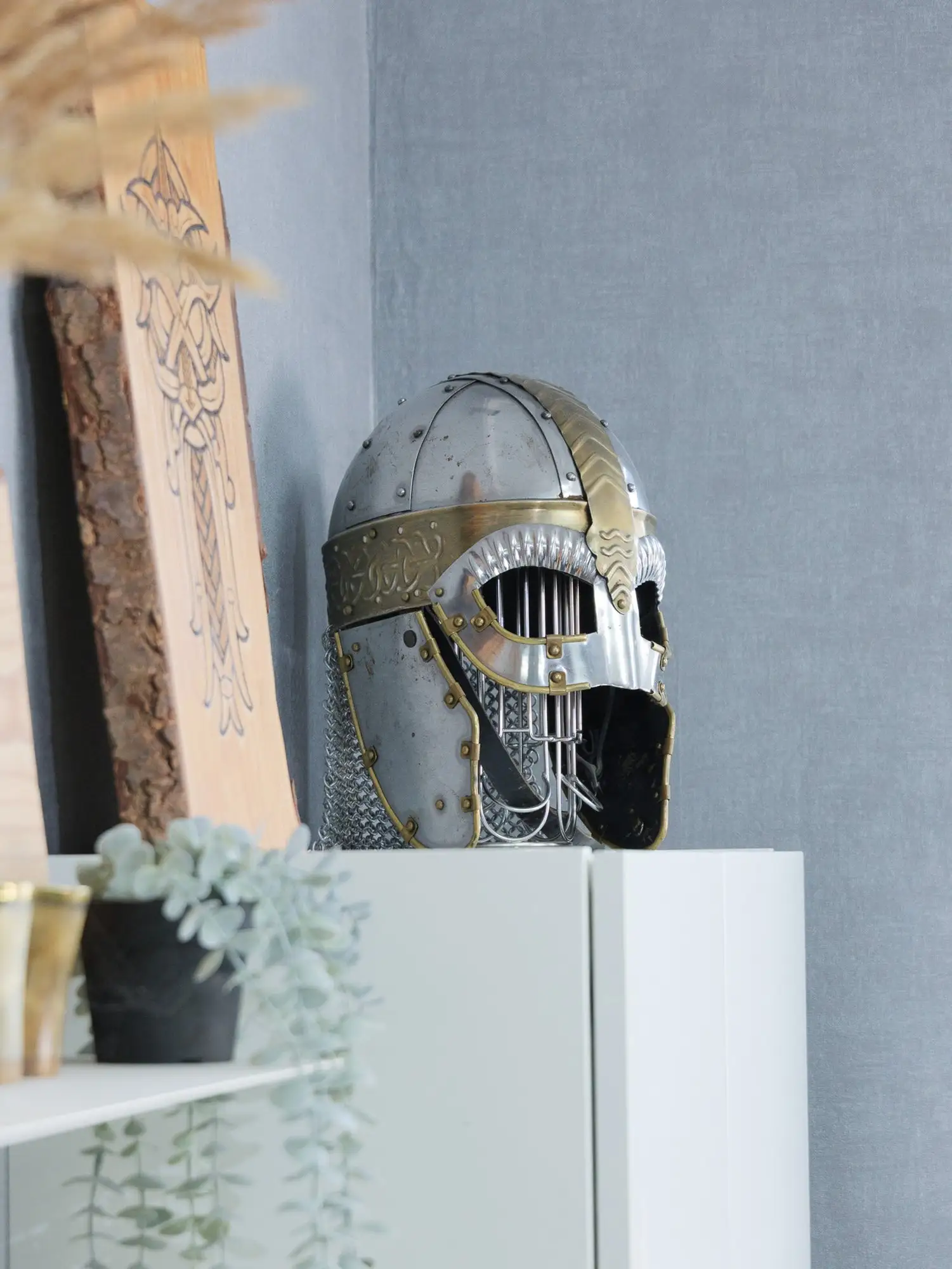 Studio-Eindruck: silberner und goldener Wikingerhelm mit Kettenhemd auf einem weißen Sideboard
