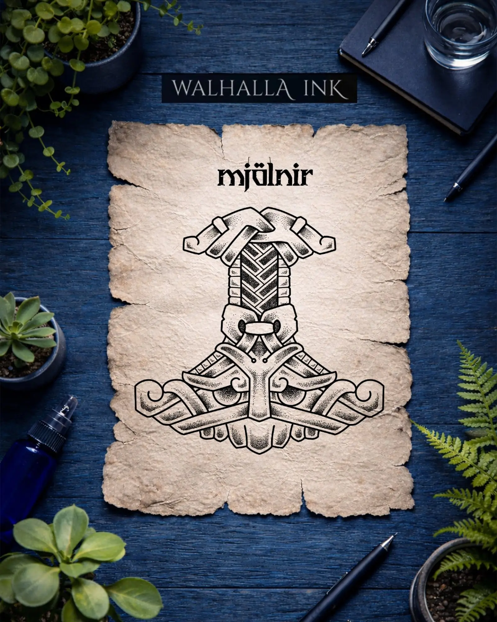 Walhalla Ink Mjölnir-Design auf Pergamentpapier, umgeben von Pflanzen, Stiften und Notizbuch.